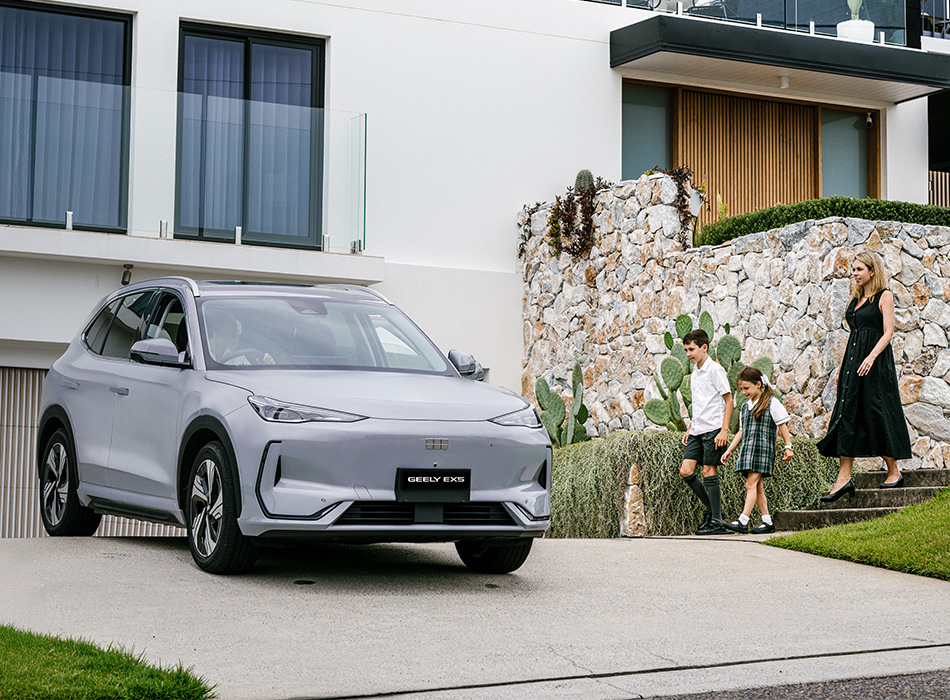 A family walking towards a silver Geely SUV parked infront of a house