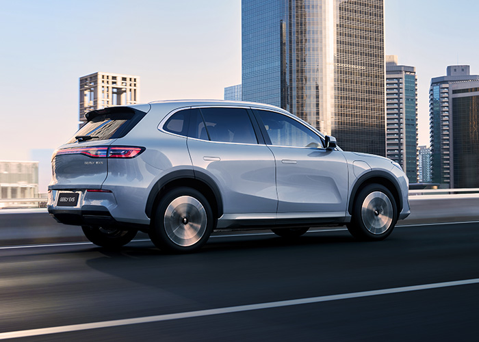 Rear side view of a silver Geely SUV driving through a city