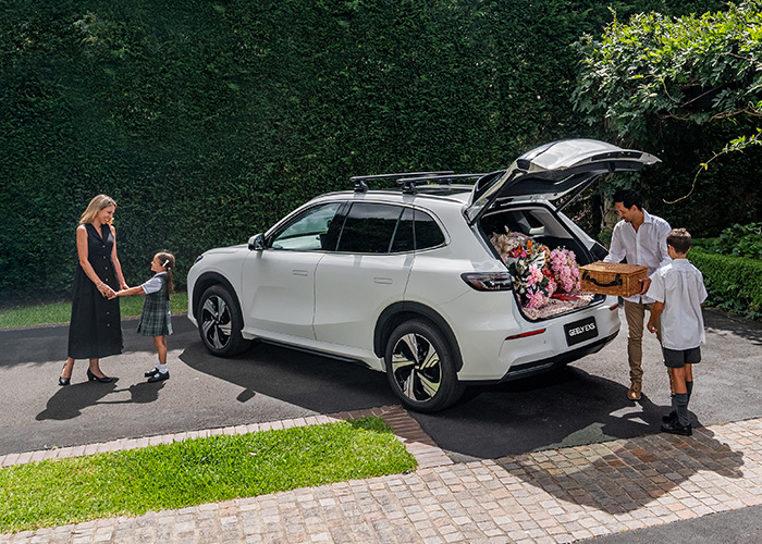 A family loading luggage into a white Geely SUV